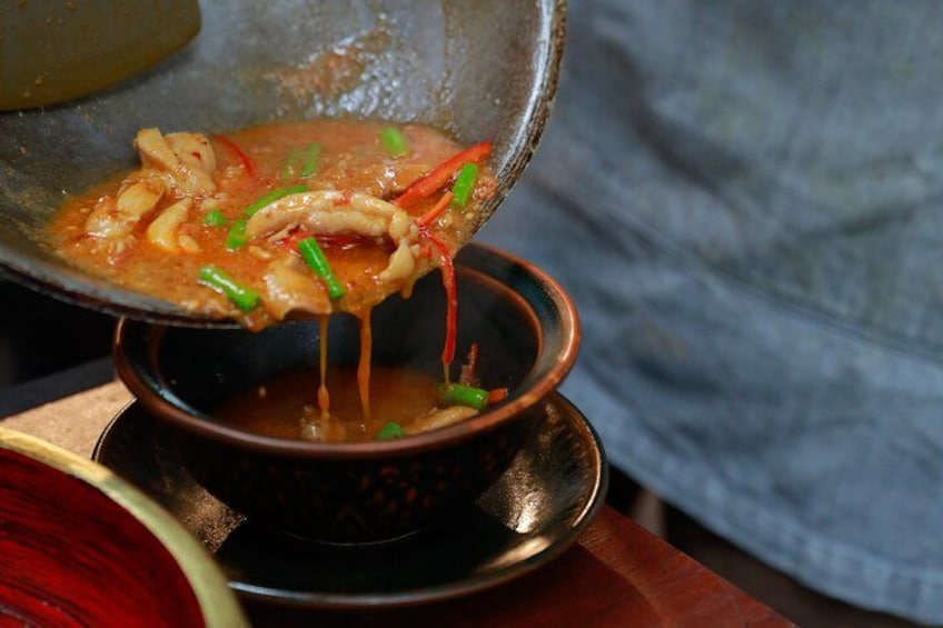 En skål suppe med en øse, pyntet med purløg og røde chilipeber. 5