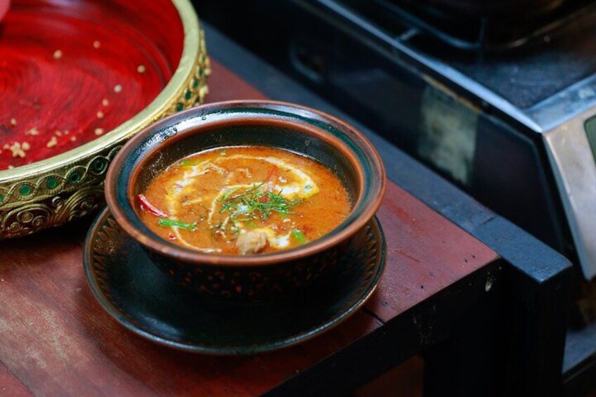 Un bol de soupe à base d’un bouillon rouge, garni d’herbes, posé sur une table en bois. 3