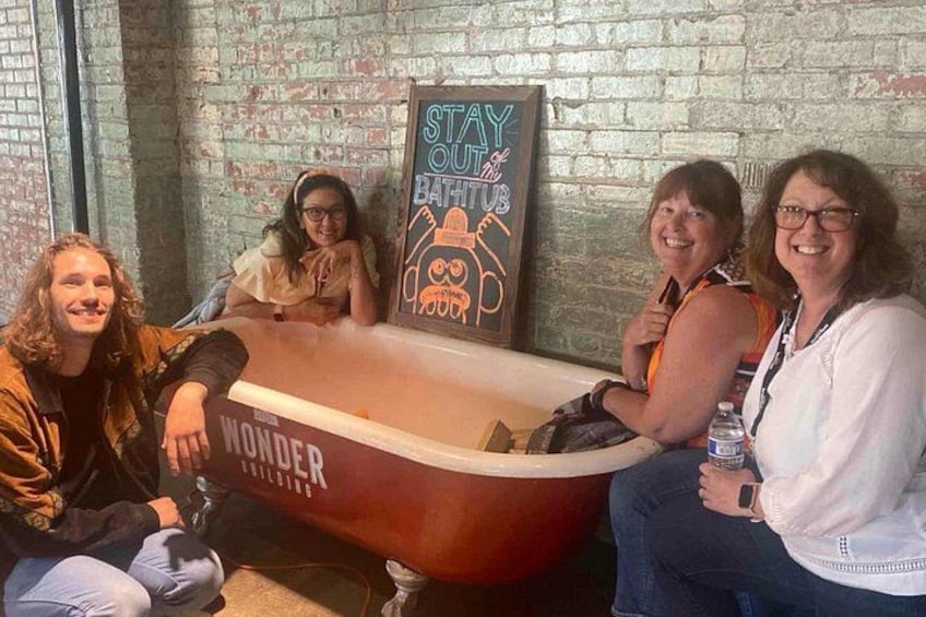 A group of people sitting around a bathtub with a sign that reads 'STAY OUT of BATHTUB.' 2