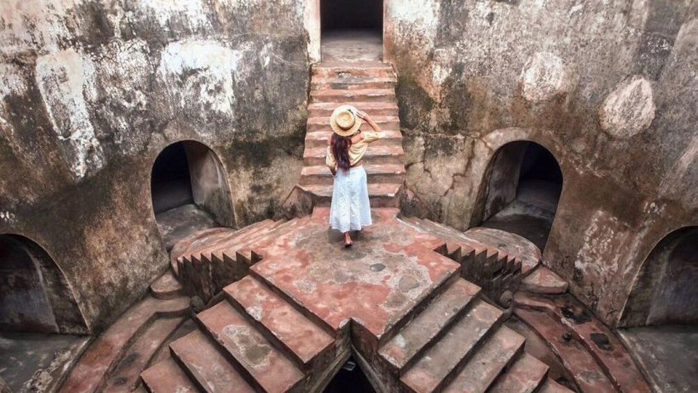 A person standing on a stone staircase between two large stone structures with arched openings. 1