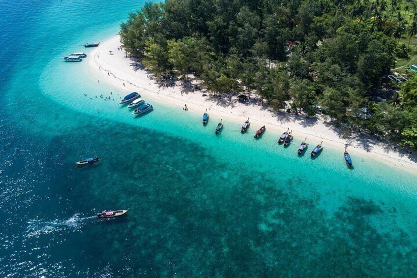 A beach with boats lined up, clear turquoise water, and a forested area. 3