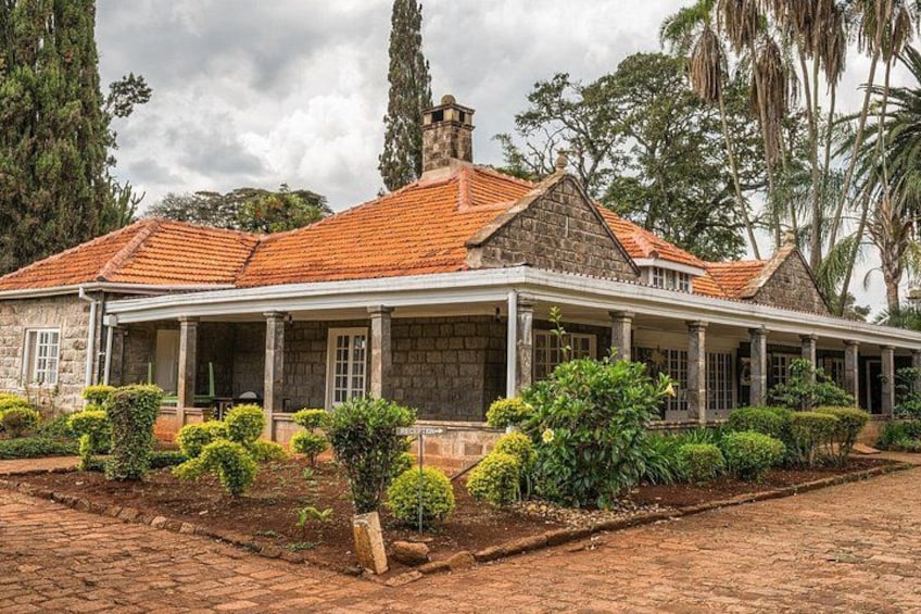 A stone house with a red-tiled roof, surrounded by well-maintained hedges and trees. 2