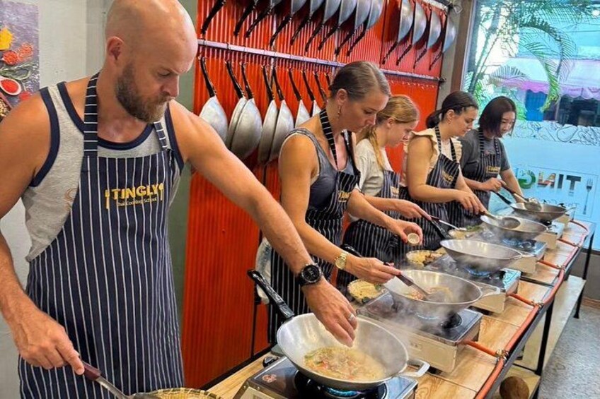 A group of people cooking in a kitchen with pots and pans on a long counter. 1