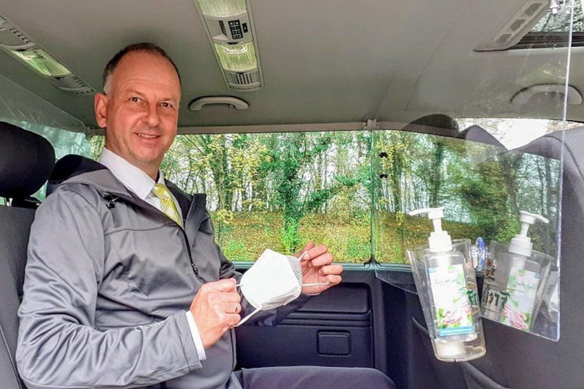A person sitting in a car holding a white object, with a window showing trees and a bottle of hand sanitizer on the dashboard. 3