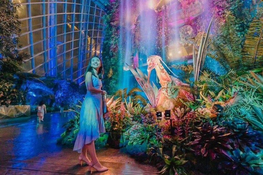 Une femme en robe, debout dans un jardin intérieur luxuriant, avec une cascade et des plantes tropicales. 5
