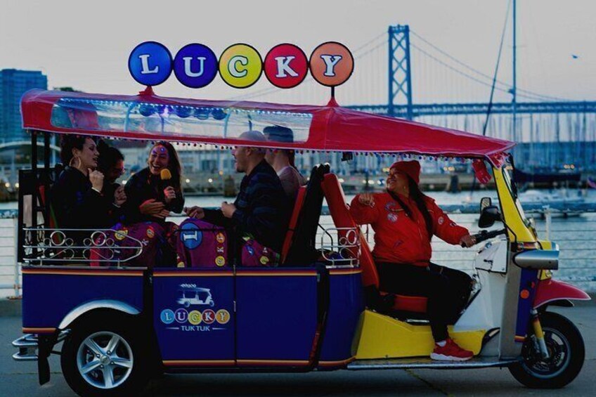 A colorful vehicle with the word 'LUCKY' on the roof, a person driving, and a bridge in the background. 2