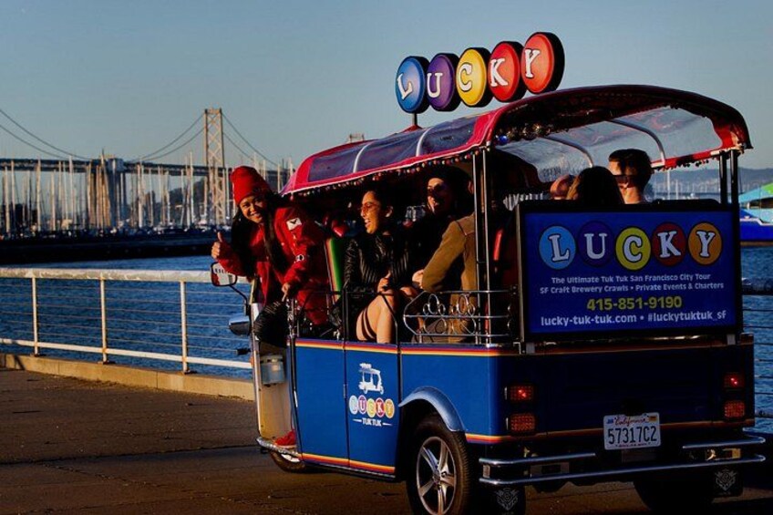 A blue tour bus with 'LUCKY' written on the side, parked by a waterfront with a bridge in the background. 3