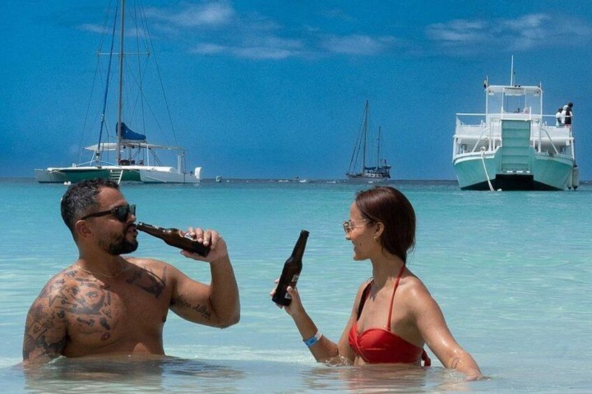 A man and a woman in a tropical setting with clear blue water, boats, and a clear sky. 5