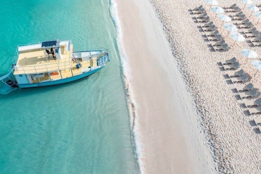 A boat on turquoise water, a sandy beach with umbrellas, and a clear sky. 3