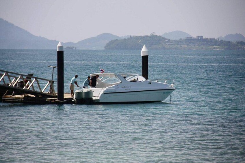 A white yacht docked at a pier with two tall poles, calm water, and a hilly landscape in the background. 2