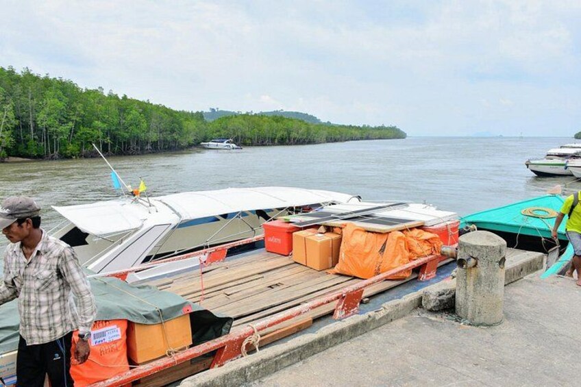 A dock with boats, a man standing, and a forested shoreline. 3