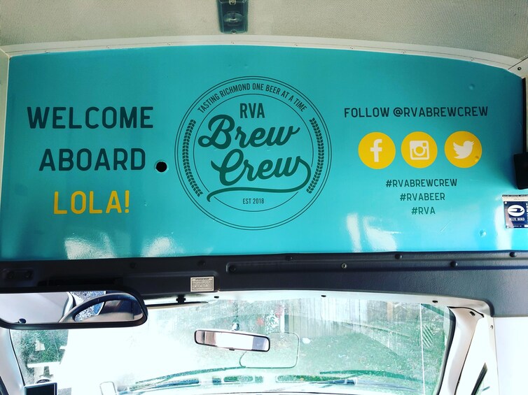 A vehicle interior with a teal-colored sign that reads "Welcome Aboard LOLA! RVA Brew Crew EST 2018" and social media icons for Facebook, Instagram, and Twitter. 5