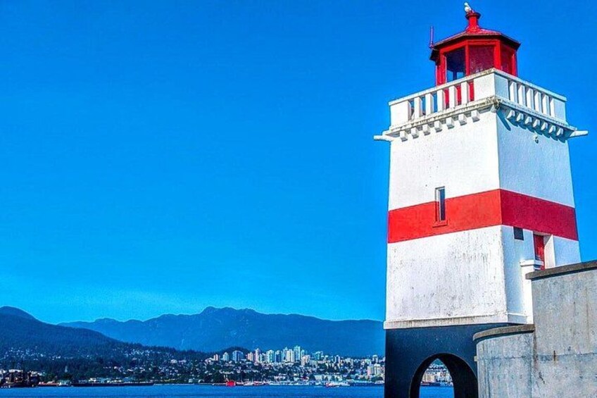 A lighthouse with a red and white color scheme, a clear blue sky, and a cityscape in the background. 2