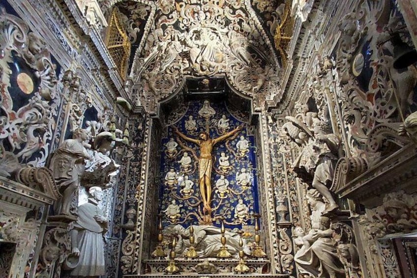 An ornate religious interior with a central crucifix, intricate carvings, and a blue and gold patterned background. 4
