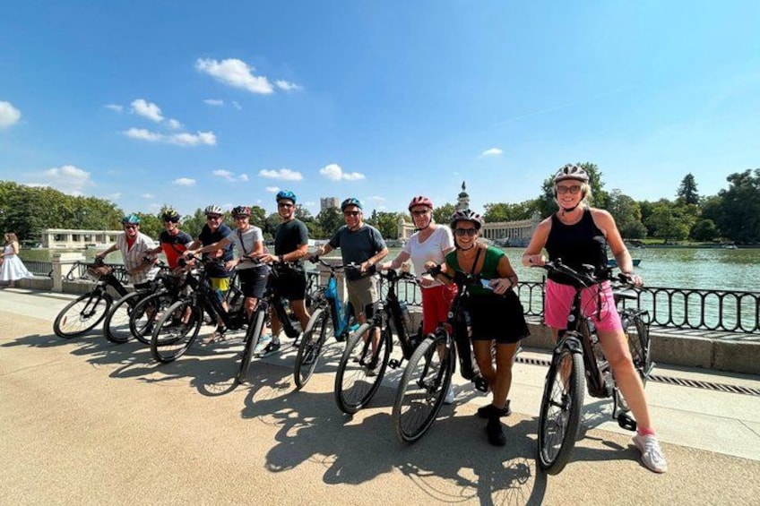 En grupp cyklister på en bro, med en flod och byggnader i bakgrunden. 1
