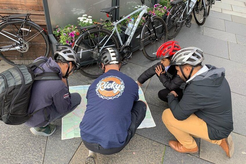 Three people sitting on the ground, looking at a map. They are wearing helmets and jackets. 2