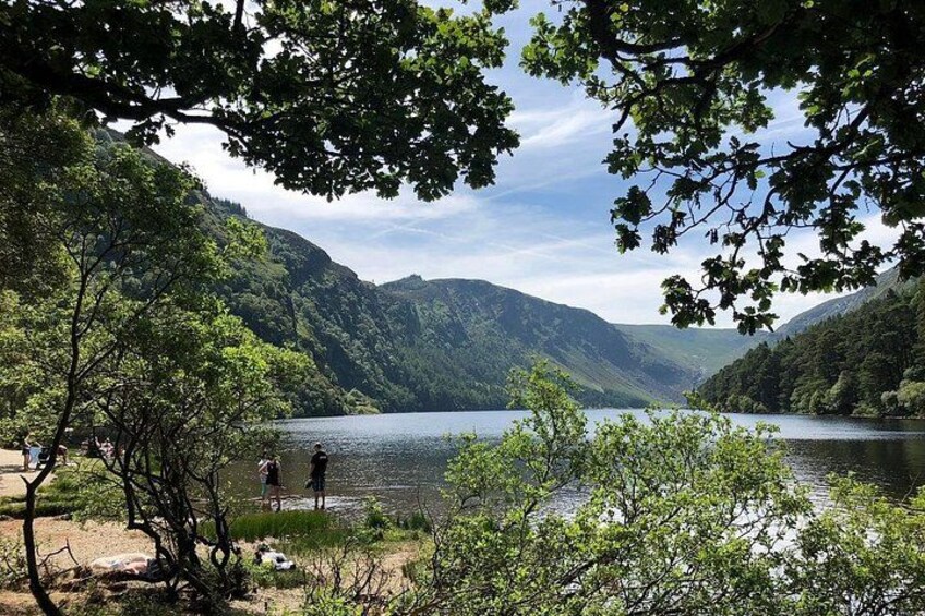 A lake surrounded by forested hills, with people walking along the shore. 2