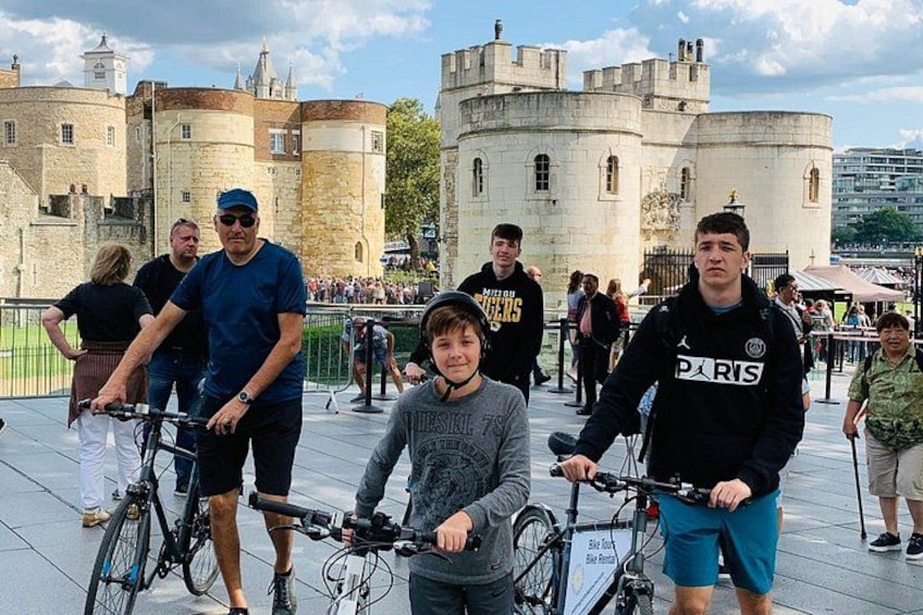 A group of people with bicycles in a historical setting with castle-like architecture in the background. 4