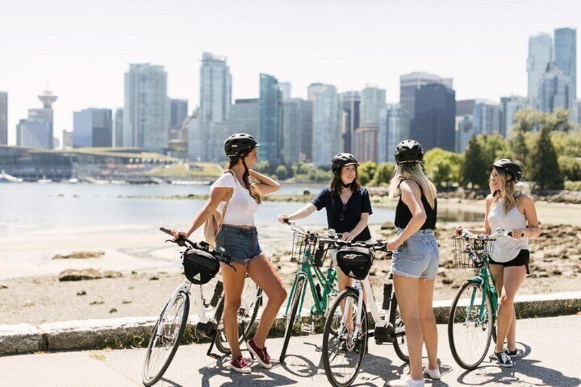 Four people on bicycles near a waterfront with a city skyline in the background. 2