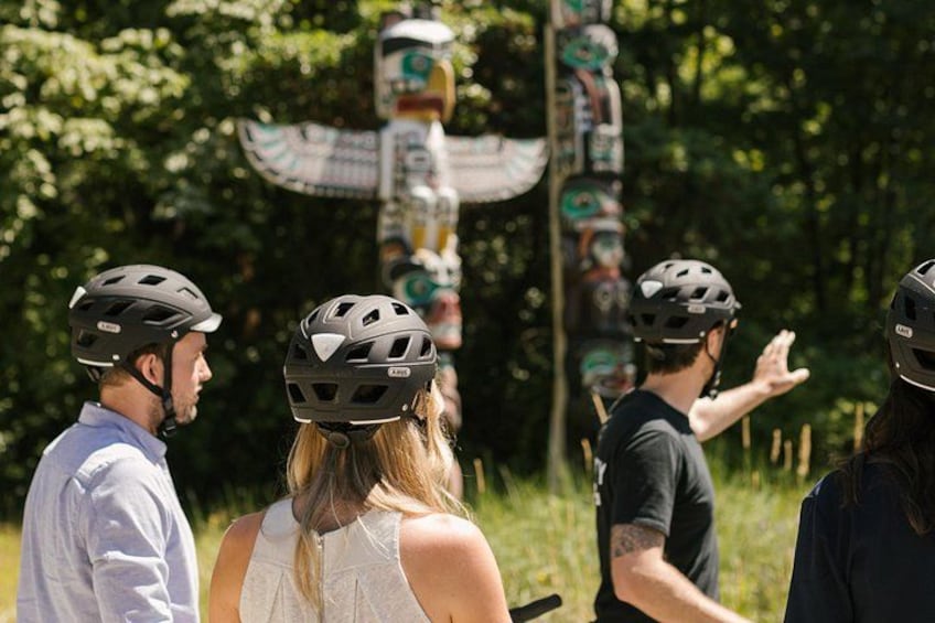 People wearing helmets, a totem pole, and a forested area. 4