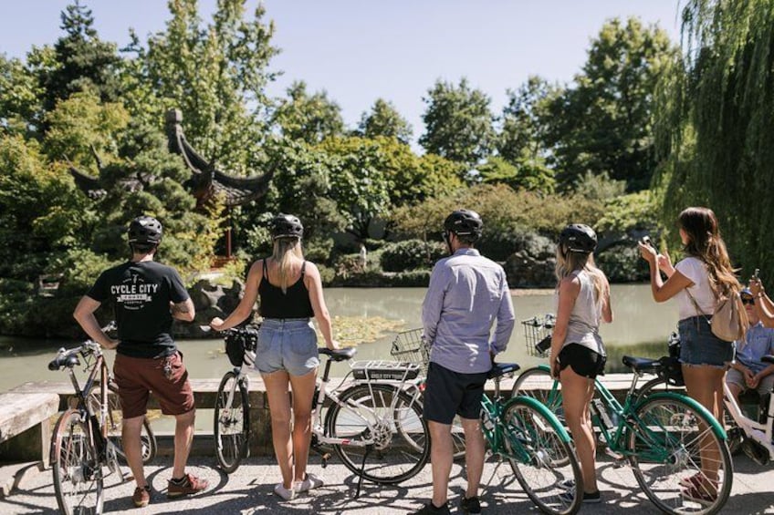 Un grupo de personas de pie junto a bicicletas cerca de un cuerpo de agua con árboles al fondo. 2