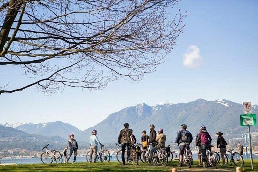 A group of cyclists on a grassy area with a lake and mountains in the background. 3