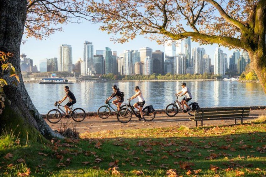 Cyclists on a path by a lake with a city skyline in the background. 2