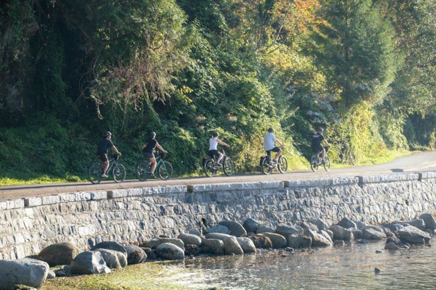 Cyclists on a paved path alongside a rocky embankment and a body of water. 1