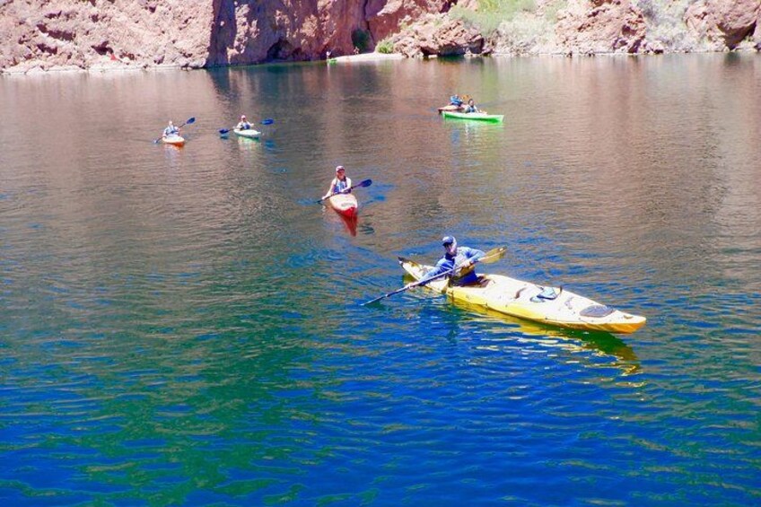 A group of kayakers on a calm lake with rocky cliffs in the background. 2