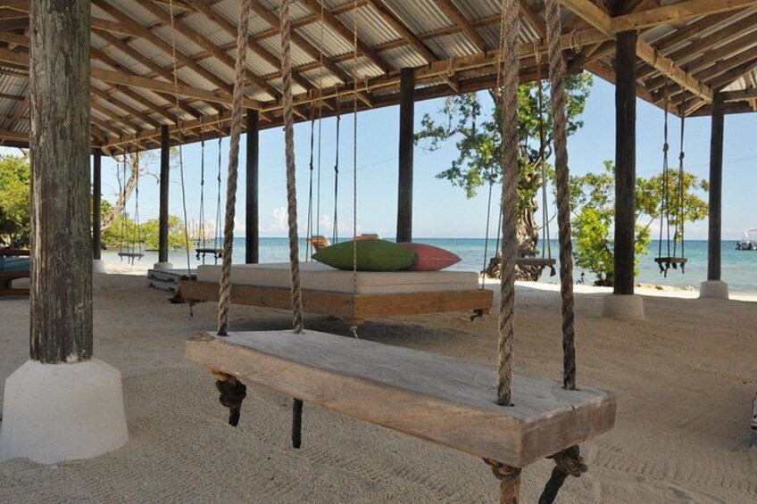 A wooden swing set with ropes, a bench, and a view of the sea. 2
