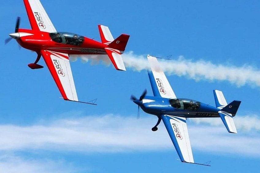 Two small aircraft flying in formation against a clear blue sky. 2