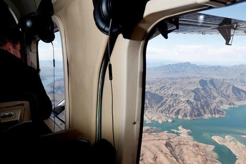 The interior of a helicopter with a view of a mountainous landscape and a body of water through the window. 2