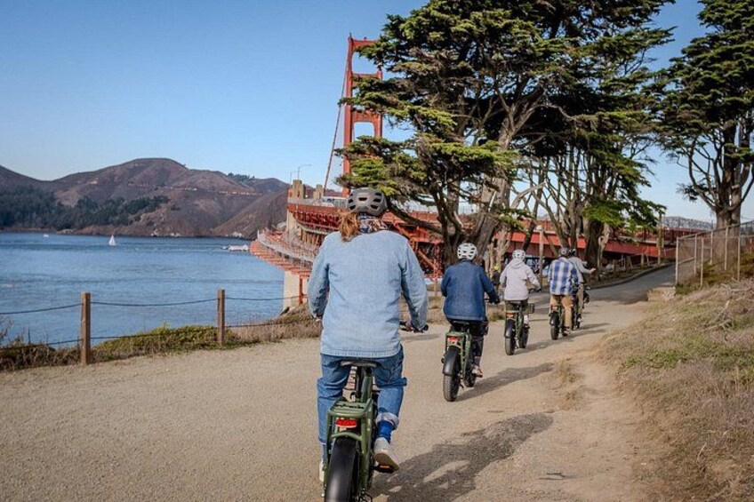 A paved path with cyclists, a body of water, and a bridge in the background. 3
