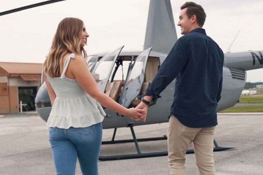 A couple holding hands in front of a helicopter on a tarmac. 2