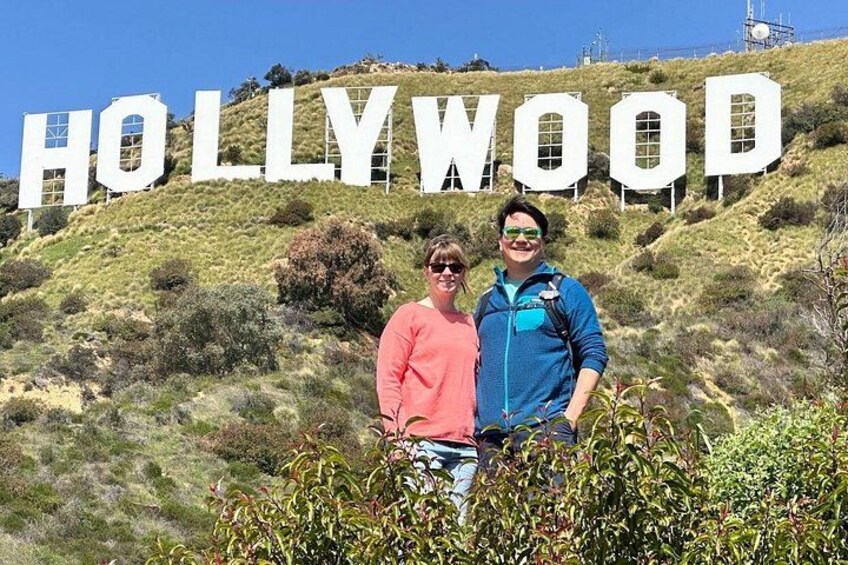 Dos personas frente al cartel de Hollywood, con un paisaje montañoso al fondo. 5