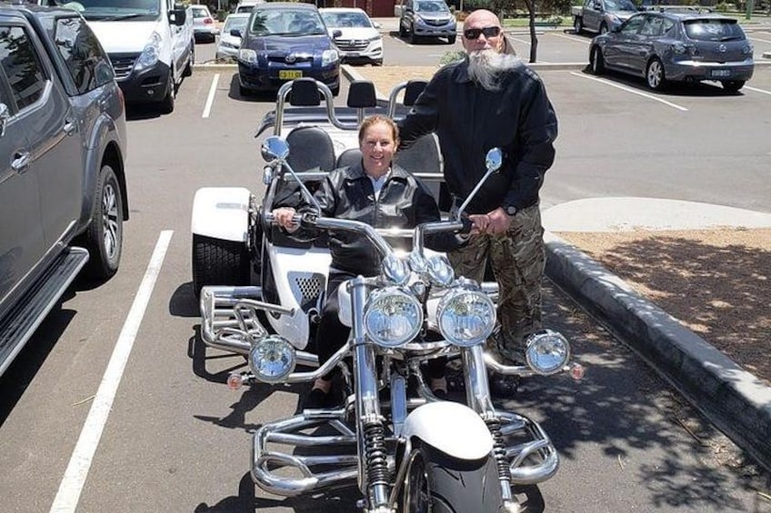 A person in a wheelchair on a motorcycle, another person standing beside it, and a parking lot with cars. 3
