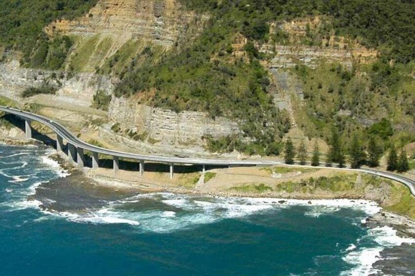 A coastal road bridge curving over the ocean, surrounded by cliffs and greenery. 2