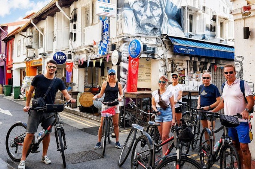 Un grupo de personas en bicicleta en una calle urbana con edificios y un gran mural. 2