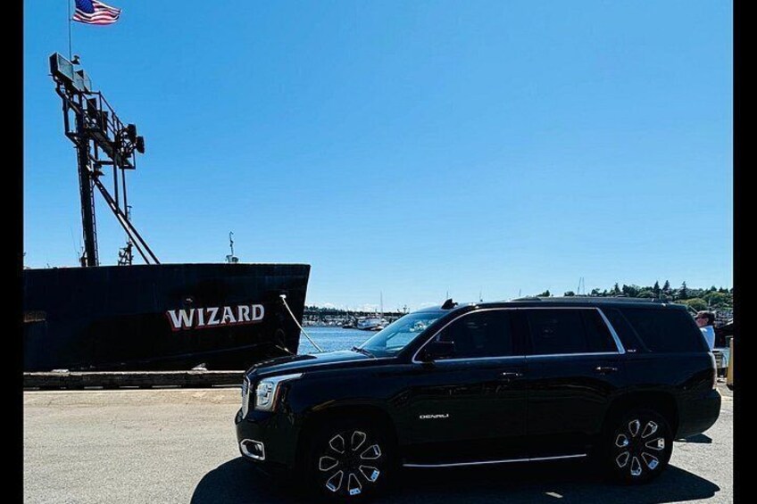 A black SUV parked near a large ship named 'WIZARD' with a clear blue sky in the background. 3