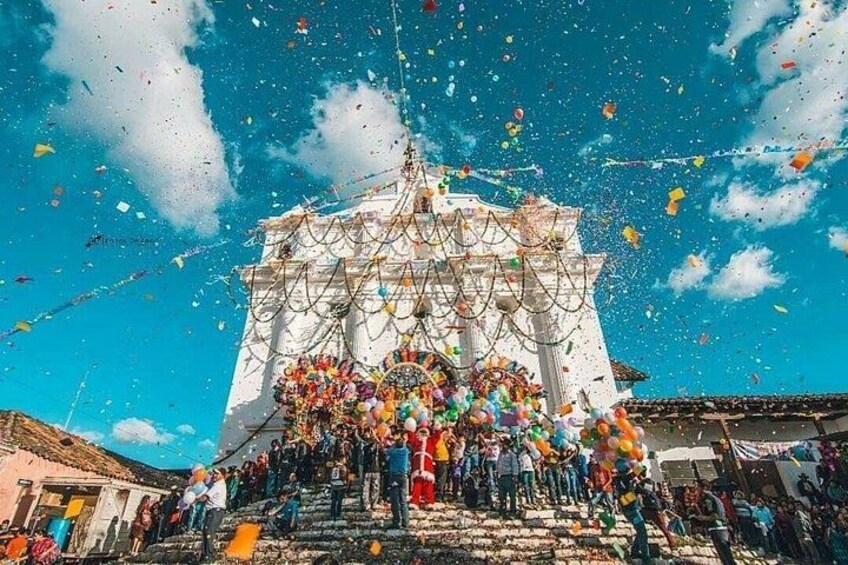 A large white building with columns, surrounded by a crowd of people and colorful balloons. 1
