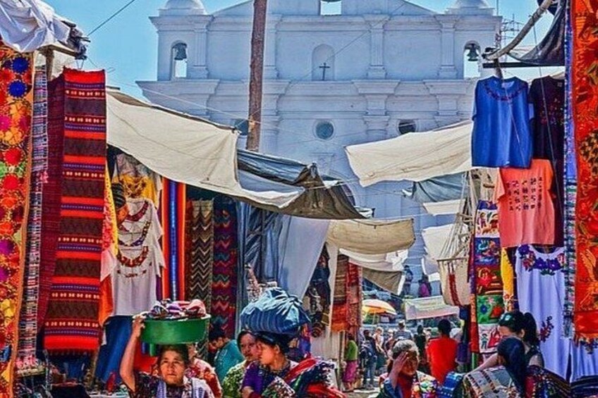 A bustling market with colorful textiles and a white church in the background. 3