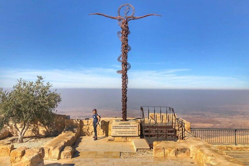 A metal sculpture with a spiral design, a staircase leading up to it, and a clear view of the landscape in the background. 3