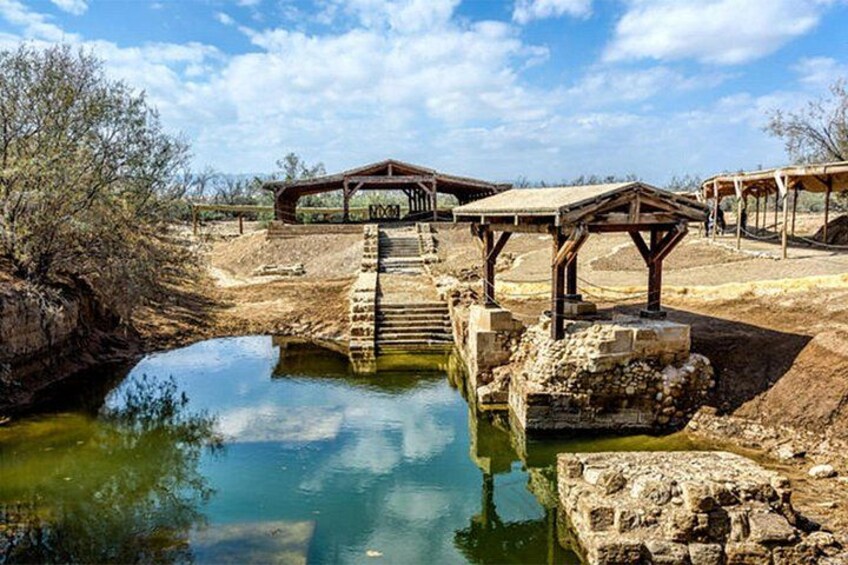 A rustic stone bridge over a calm water body, wooden gazebos, and a dry, arid landscape. 2