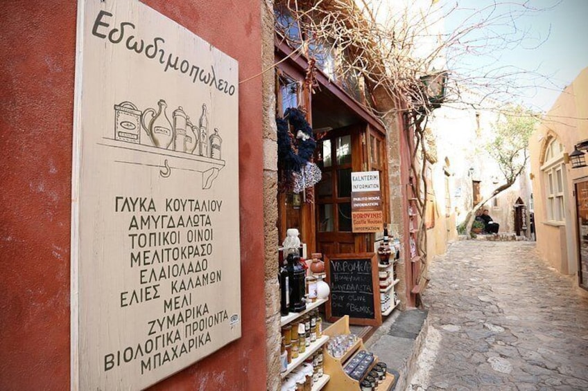 A narrow street with a shop displaying various items and a signboard listing products. 5