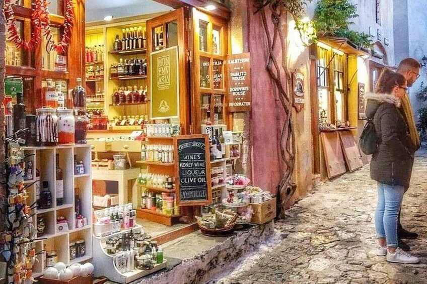 A storefront with wooden shelves stocked with various products, a signboard with text, and a tree growing through the entrance. 1