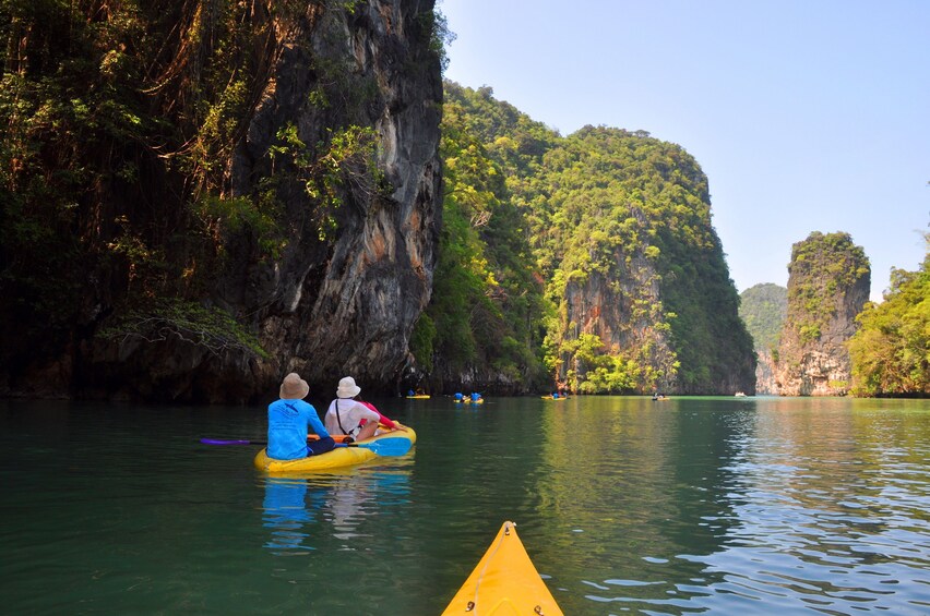 Two people kayaking on a calm river surrounded by lush green cliffs. 4