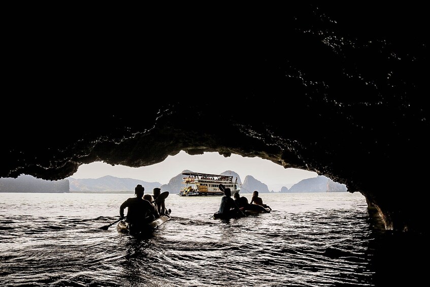 A group of people in a boat near a cave entrance with a boat in the background. 2