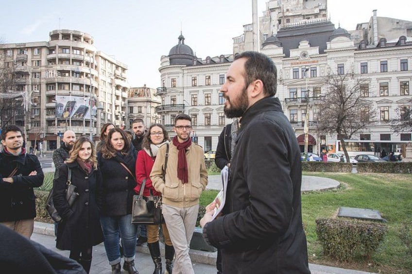 A group of people standing outdoors in an urban setting with historical buildings in the background. 5