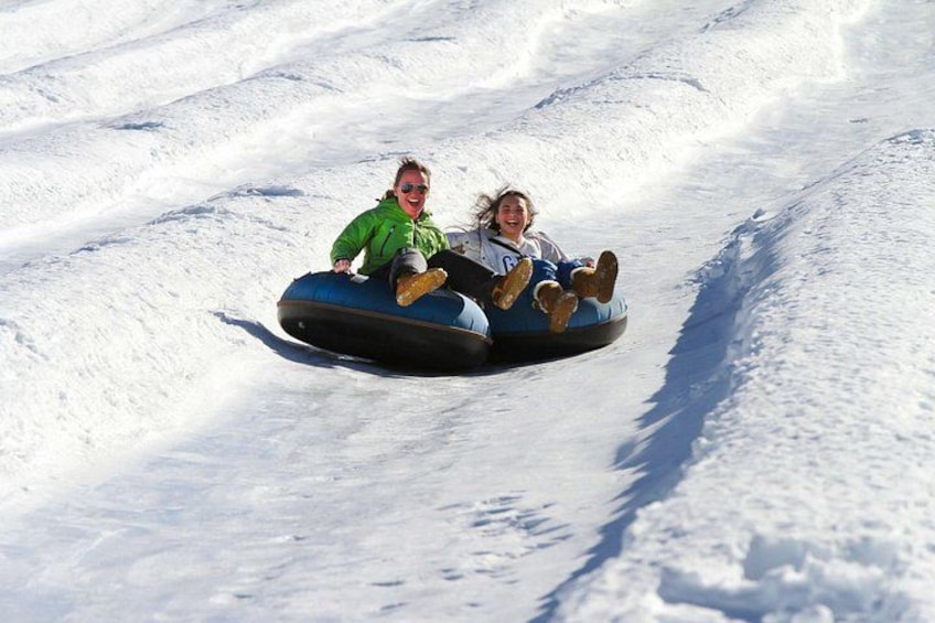 Two people on a snow tube in a snowy slope. 3