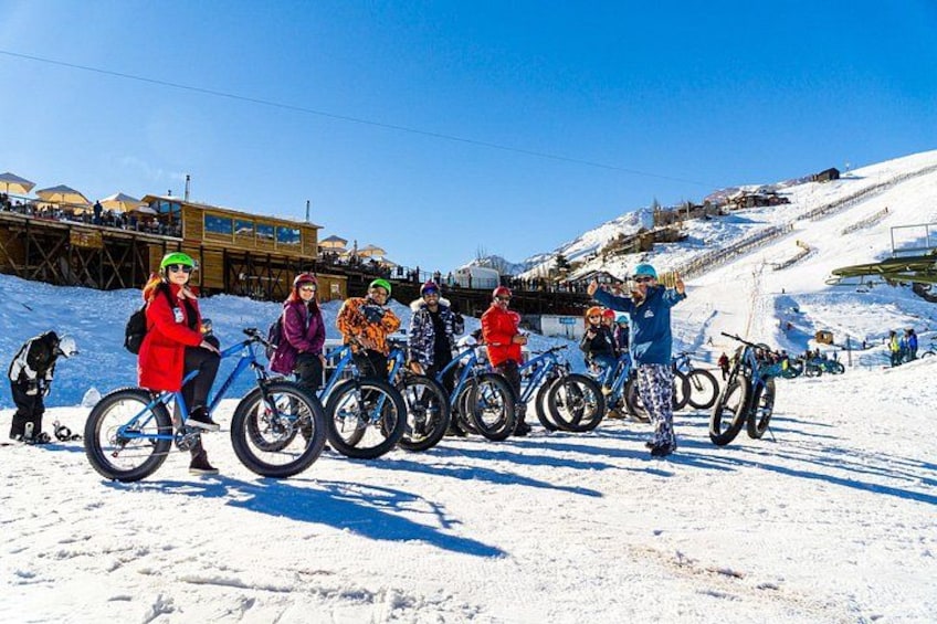 A group of people on bicycles on a snowy slope with a ski lift in the background. 5